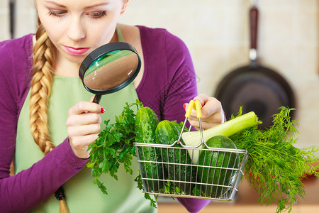 购买健康的饮食品概念厨房里的女人有很多绿色蔬菜她们通过放大镜看购物篮小车女人通过放大镜看蔬菜篮图片