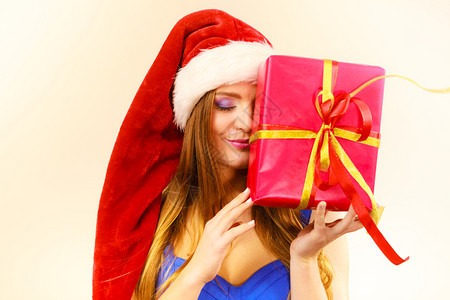穿着圣达克萨斯帽子的可爱女人拿着大红色的圣诞礼物把她的脸藏在礼物后面圣诞幸福冬天和人的概念圣达克萨斯帽子的女人拿着礼物盒圣诞节时图片