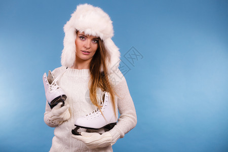 穿着温暖的帽子和舒适白衣女孩穿着冰鞋蓝背景工作室拍摄戴冬帽的妇女穿着冰鞋图片