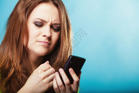 愤怒的困惑少女孩在手机上发短信使用智能手机在蓝色上读写短语图片