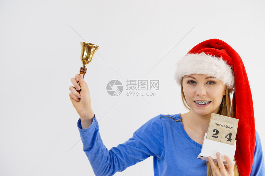 带着圣诞老人的帽快乐年轻少女拿着日历12月4日的约会和钟声圣诞女人拿着日历和钟声图片