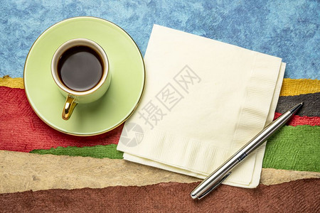 餐巾纸笔和一杯咖啡与用纸质的彩色手工造纸所创的抽象景观相对图片