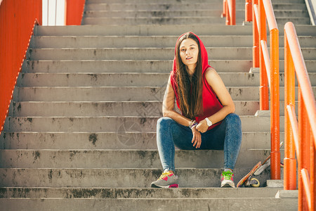 酷的溜冰运动员长发女孩坐在城市的楼梯上滑板坐在城市的楼梯上活跃的生方式在夏天很怪异户外运动潮流的青少年滑板女孩坐在楼梯上图片