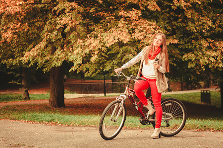 美丽的女子在户外的秋季公园骑自行车图片
