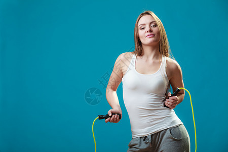 穿着运动服的美丽快乐女孩在蓝背景上跳过绳子图片