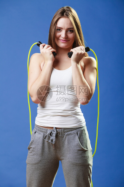 穿着运动服的美丽快乐女孩在蓝背景上跳过绳子图片