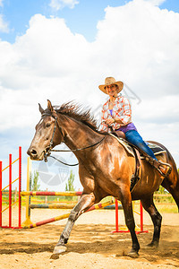 牛仔帽女在阳光明媚的白天骑马穿越障碍图片