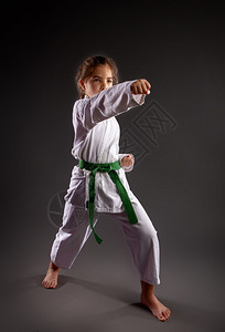 一个女孩在传统的白色和服中用空手道和绿带在黑暗背景下开展训练演习图片