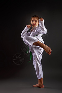 一个女孩在传统的白色和服中用空手道和绿带在黑暗背景下开展训练演习