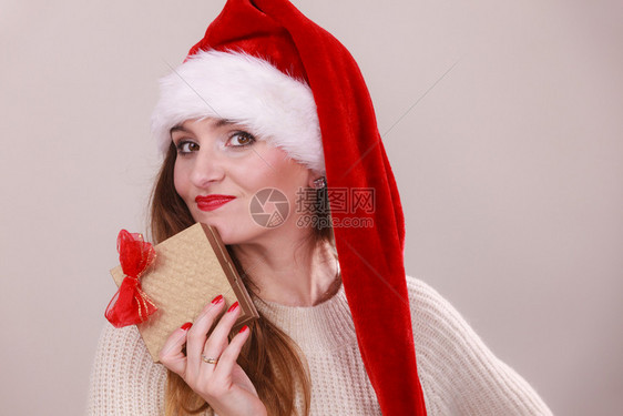穿着圣达克萨斯帽子的快乐女人拿着红弓的金礼盒圣诞节时间赠与和幸福的概念拿着礼物盒的女人图片