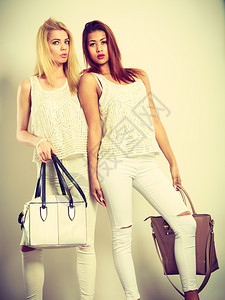 女士时装服饰两名年轻模特用手提包拍的照片身着白衣服的迷人女孩身着手袋的年轻模特图片
