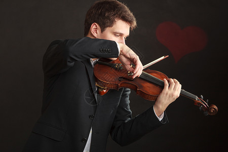 音乐激情爱好概念浪漫青年男子穿着优雅的木小提琴演奏工作室用红心在黑暗背景中拍摄男子穿优雅的小提琴演奏图片
