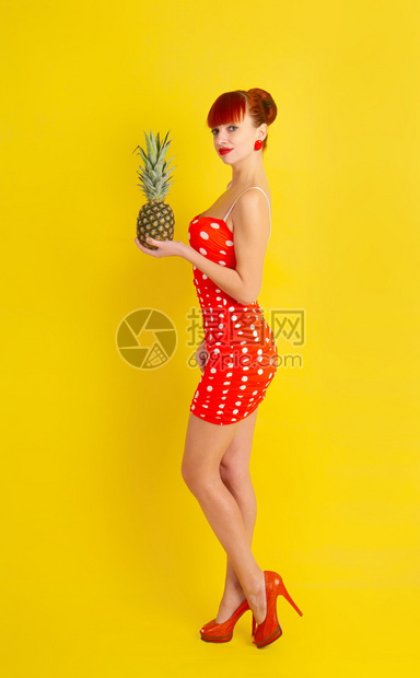 穿着波卡点装的红头发漂亮女孩手里拿着菠萝黄褐色的背景图片