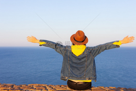 穿着旅行服和帽子坐着看蓝色的海洋和天空旅行概念照片穿旅行服和帽子坐着看蓝色的海洋和天空图片