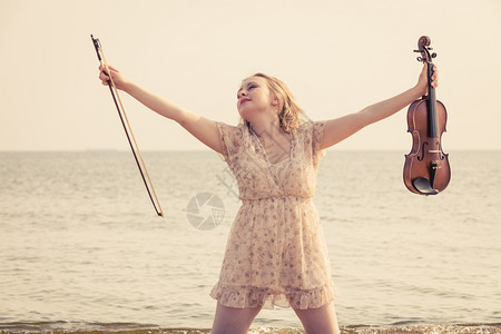 在海边的滩上妇女拿着小提琴享受她的爱好在海边滩上妇女拿着小提琴图片