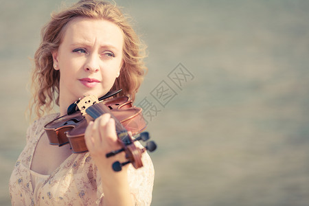 在海边滩上玩小提琴的妇女在沙边小提琴上玩的妇女图片