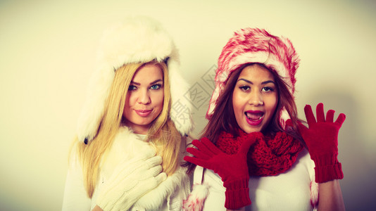 时装冬季饰概念两个金发女孩和黑穿着温暖的红白衣服玩得开心两个女孩穿着毛帽围巾手套有吸引力两个女孩穿着温暖的冬装玩得开心图片