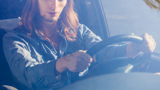 年轻男子穿着牛仔裤衬衫长发驾驶汽车图片