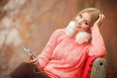 数字设备外面的学生带手机年轻女坐在公园长椅上的迷人女孩秋季天气带手机的年轻女图片