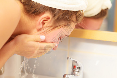在浴室用清洁水洗脸的妇女照顾外衣的孩早间卫生皮肤护理治疗在浴室洗脸的妇女卫生图片