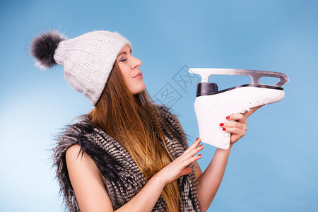 冬季体育活动概念身着温暖帽子和毛皮外衣的女孩拿着看滑冰蓝背景工作室拍摄的镜头身着冬帽的妇女看滑冰图片