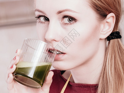 厨房的年轻女子拿着绿色健康的蔬菜果汁杯厨房的妇女拿着蔬菜汁图片