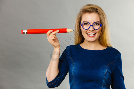金发女学生孩或教师拿着大红铅笔绘画工作室拍摄在灰色上微笑的女人手握着大铅笔图片