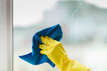 女用黄色手套蓝抹布和喷雾洗涤剂用黄色手套打扫窗户春季清洁家务工作概念使用洗涤剂擦家庭窗户图片