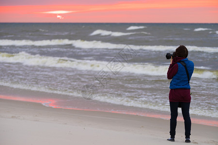 在秋天的气下妇女闲暇时间在海岸线上走动用照相机拍背景图片