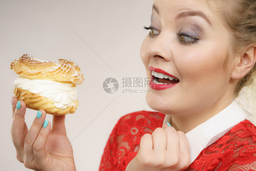 快乐的金发女人拿着美味甜果饼奶油兴奋的面容表情灰色的有趣女人拿着奶油泡芙饼图片