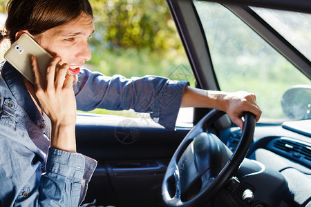 年轻人驾驶汽车时使用智能手机与人交谈图片