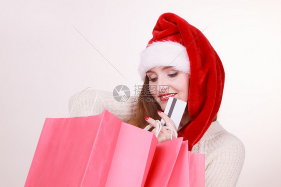 身戴圣达克萨斯帽子持有红色购物袋和信用卡购买礼品戴圣诞帽的妇女持有信用卡和购物袋图片