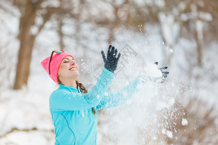 玩雪在冬季公园放松的年轻女健康自然的时装身概念女孩在周围吹雪背景