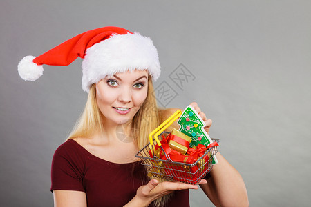 戴圣诞老人帮手帽子的快乐妇女拿着小圣诞树和里面的礼物购篮车图片