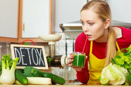 厨房的年轻女子在脱毒标志旁边拿着绿色健康的蔬菜冰淇淋汁杯图片