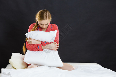 患有抑郁症的年轻女子金发孩穿着红色睡衣坐在枕头的床上深黑夜背景图片
