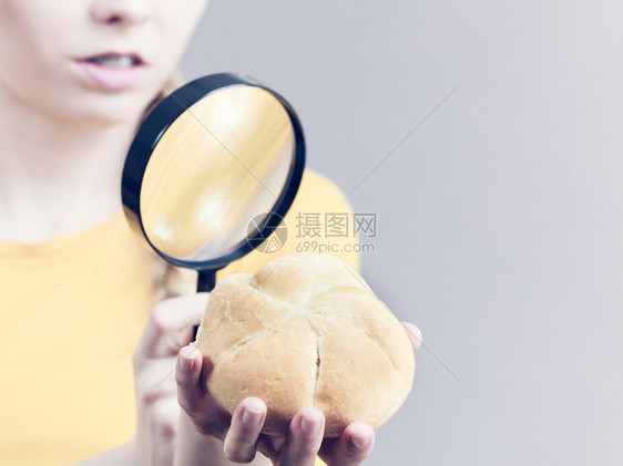 持有面包卷和放大镜的妇女检查小麦产品成分图片