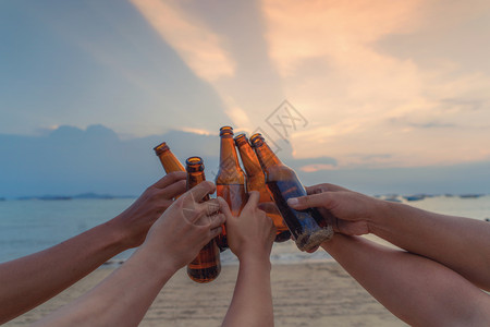 朋友亲手近地把啤酒瓶连在一起夏天日落时海滩或边庆祝节日图片