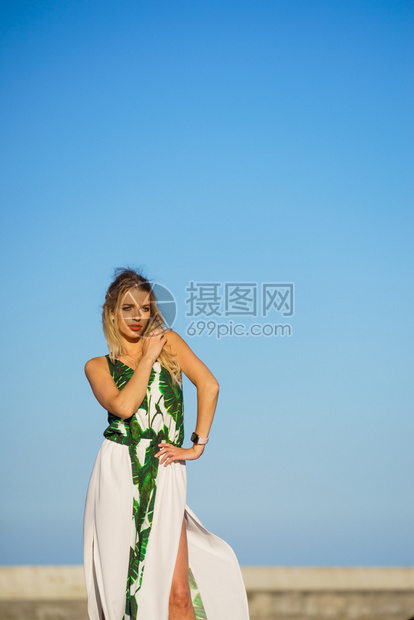 美丽的时装模特儿与蓝晴的天空对抗漂亮的金发年轻成女子穿着长的白色绿夏裙图片