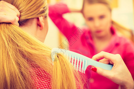 女人在浴室梳长金发的光滑头看着镜子早上少女在清新发型时照顾她们理发概念女人在浴室梳长发图片