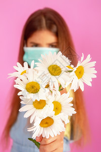有过敏的小女孩穿着医用面罩花朵的过敏小姑娘带着温柔粉红背景的花束图片