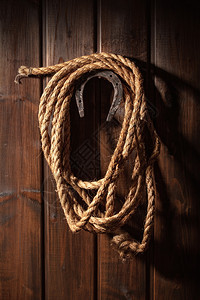 一只老马蹄铁挂在一根钉子上用拉索套在黑木墙上马蹄铁和拉索图片
