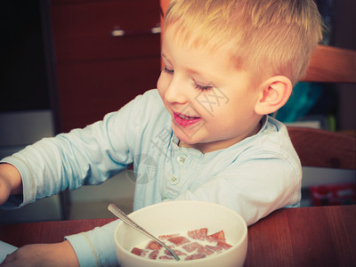 男孩吃早餐麦片和碗中的牛奶图片