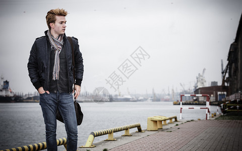年轻英俊男子时尚型随身便式袋装在街头城市工业背景上图片
