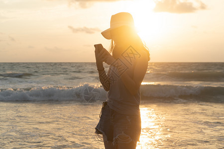 快乐的亚洲妇女使用手机或在海滩上社交媒体发短信图片