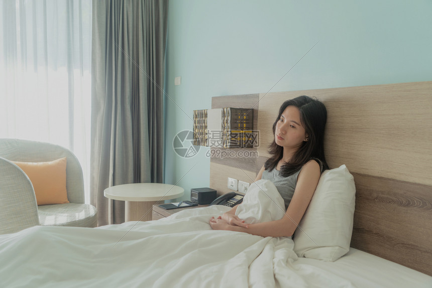 亚裔女在现代卧室里穿着白色毯子思考问题且在床上患忧郁症图片