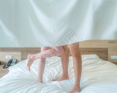在现代卧室里,浪漫夫妇双腿站在床上,带着白毛巾和爱性观念的毯子。图片