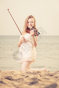 音乐爱好和日常激情概念海边滩上的妇女玩小提琴在海边滩上的妇女拿着小提琴图片