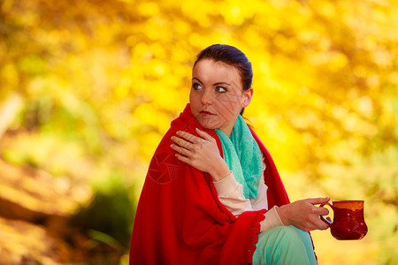 秋天公园的深思熟虑女人在享受热饮咖啡或茶拿着红杯加热饮料的休闲娱乐中放松黄叶背景图片