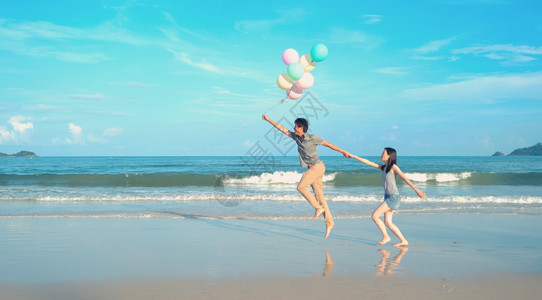 快乐的亚洲情侣在泰国普吉Phucket中午的海洋或自然度假室外旅行时在海滩上持有彩色气球背景图片